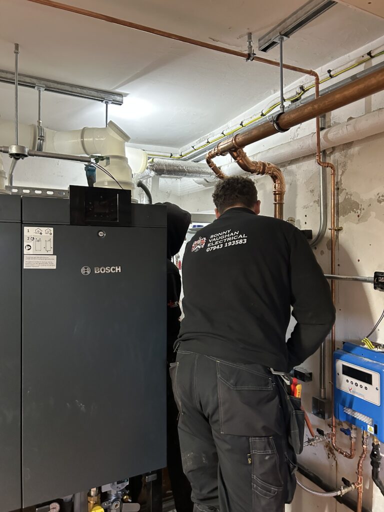 Electrician in Sonny Vaughan Electrical uniform with his back to the camera. He is in a boiler room, fault finding.