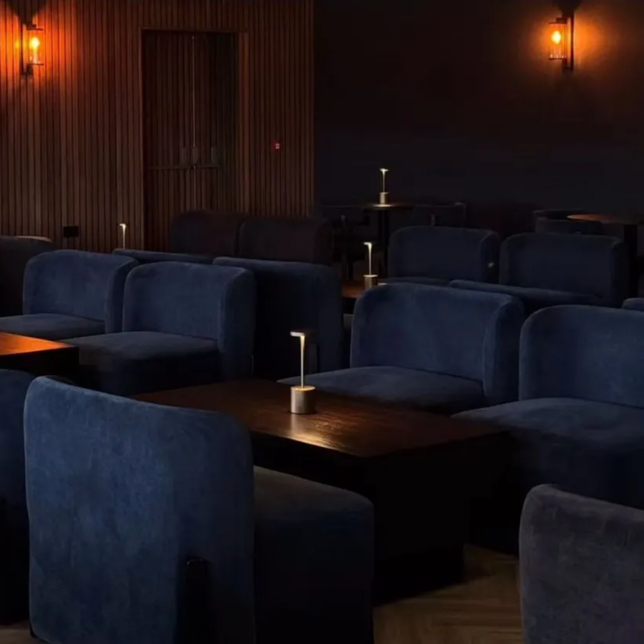 Home Modern private function room in Bangor city stadium. There are rows of navy plush chairs in between oak tables. The room is dimly lit with orange lights.