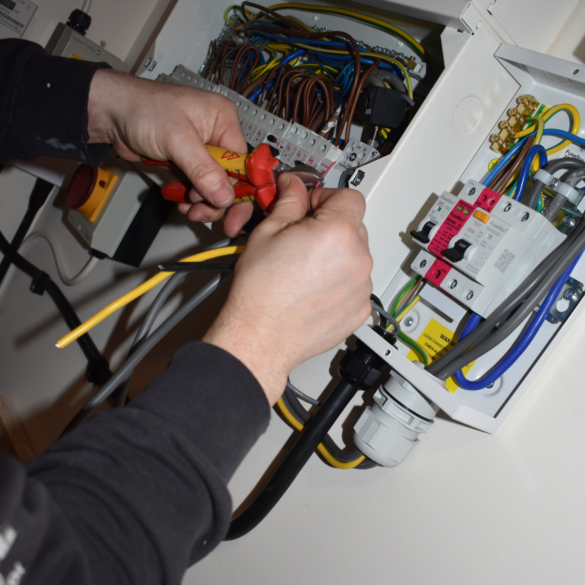 Home Zoomed in image of open distribution board with electrician's hands testing the wires.