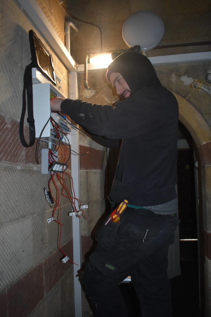 Electrician in dimly lit church room changing distribution board