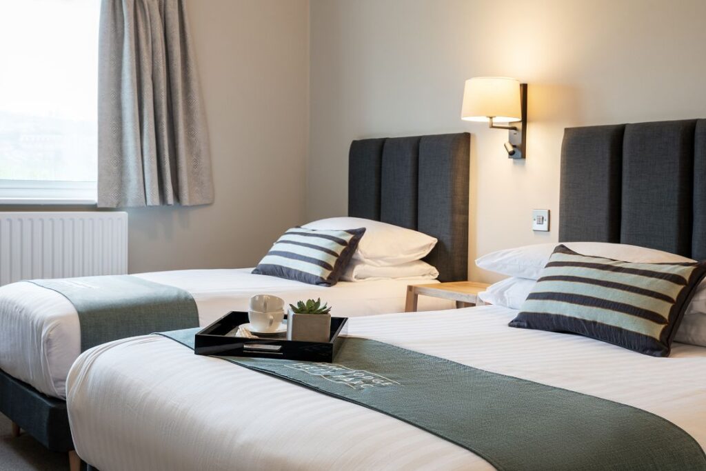 Modern refurbished hotel bedroom with a refreshment tray on the bed.